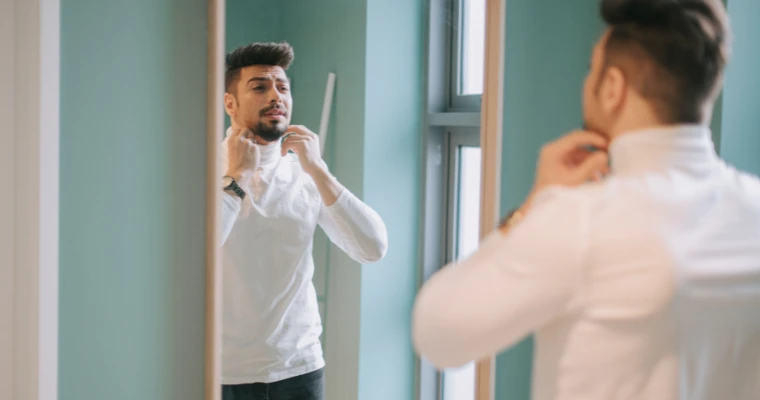 Homem olhando no espelho e se arrumando, demonstrando amor próprio