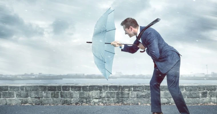 Homem sendo resiliente e se protegendo de um vento forte e chuva com um guarda chuvas.